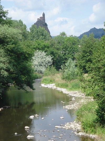 Cours d'eau dans la végétation avec le pic du Puy-en-Velay au loin